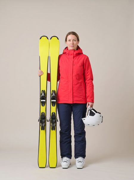 A woman in a red jacket beside yellow skis stood on their tails, reaching her forehead
