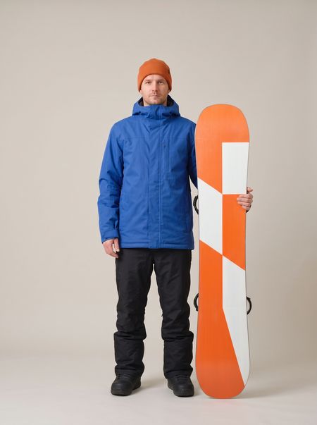 A man in a blue jacket beside an orange snowboard stood on its tail, reaching his chin