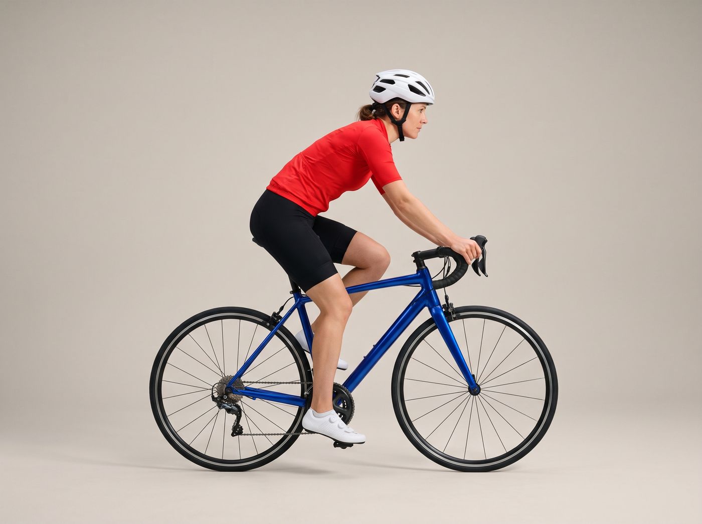 A woman in a red jersey riding a blue road bike, seen from the side, with her leg almost straight at the bottom of the pedal stroke