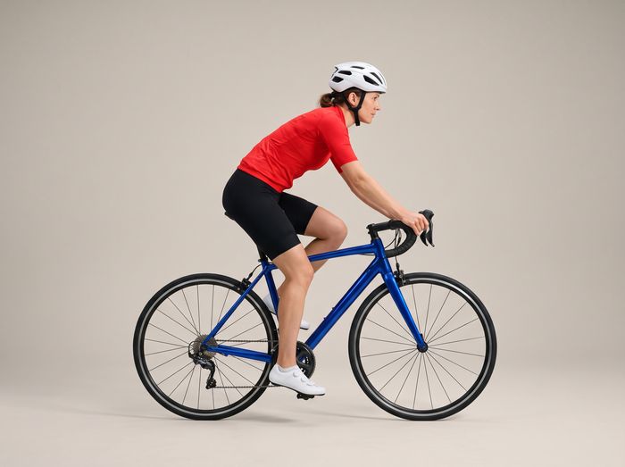 A woman in a red jersey riding a blue road bike, seen from the side